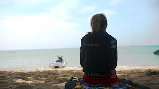 Rear View Of A Girl In A Hoodie Sitting On The Beach And Watch The Sea, Blue Sky And Sea Background