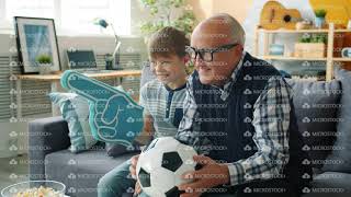 Joyful family grandfather and grandson watching football on TV cheering hugging