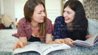 Two young woman friends are watching magazine on bed in bedroom at home