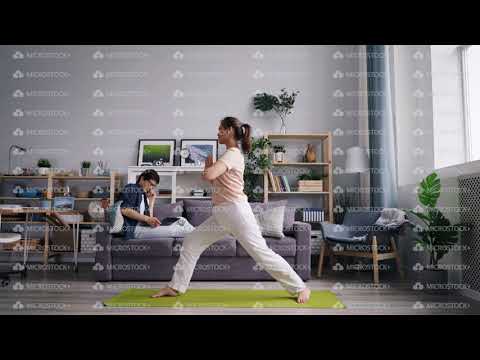 Female student doing yoga while husband working with laptop talking on phone