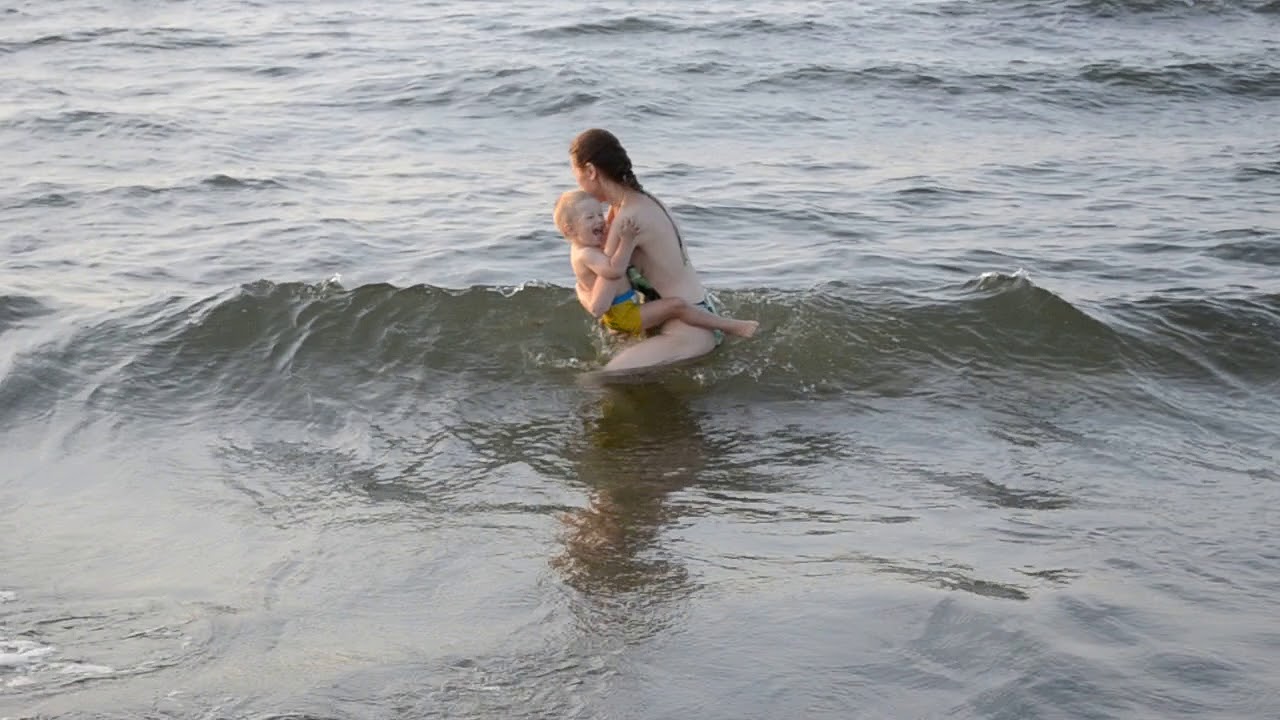 Голая нудистка на прибережных скалах принимает волны воды на тело