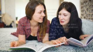 Two young woman friends are watching magazine on bed in bedroom at home