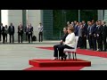 Angela Merkel sits for military honours after being seen shaking three times