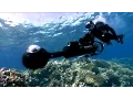 A diver swims underwater with a large camera in hand