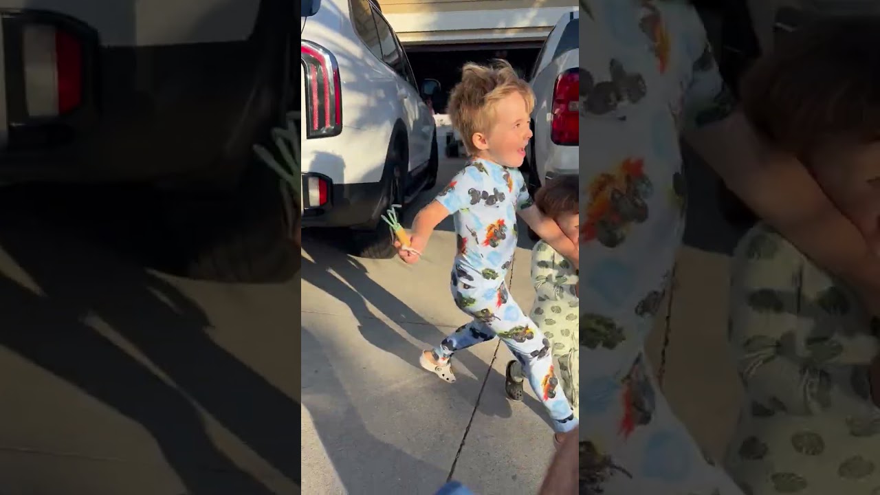 Boy holding toy runs in driveway and crashes into little brother after walking between to SUV cars