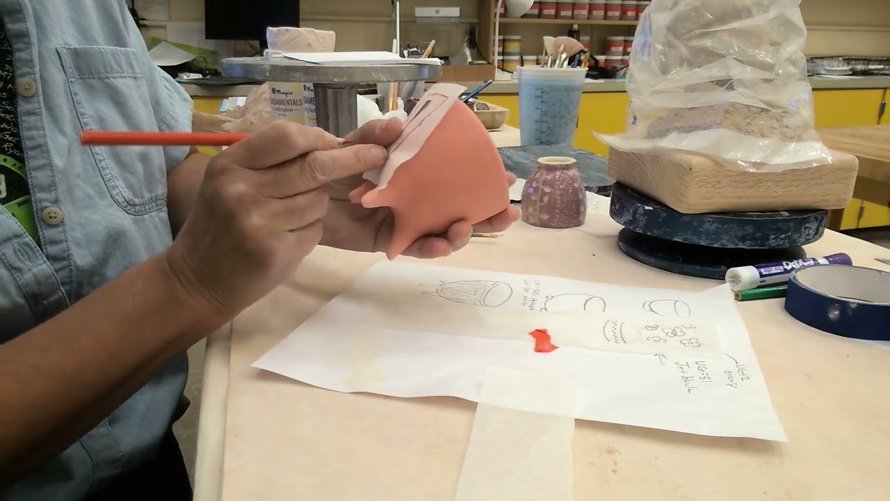 Video thumbnail of a potter carving into a small leather hard cup held in one hand, with pencil sketches on the table