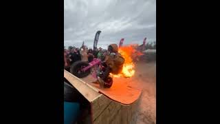 Guy rides motorcycle while jacket is on fire up ramp then lands into water