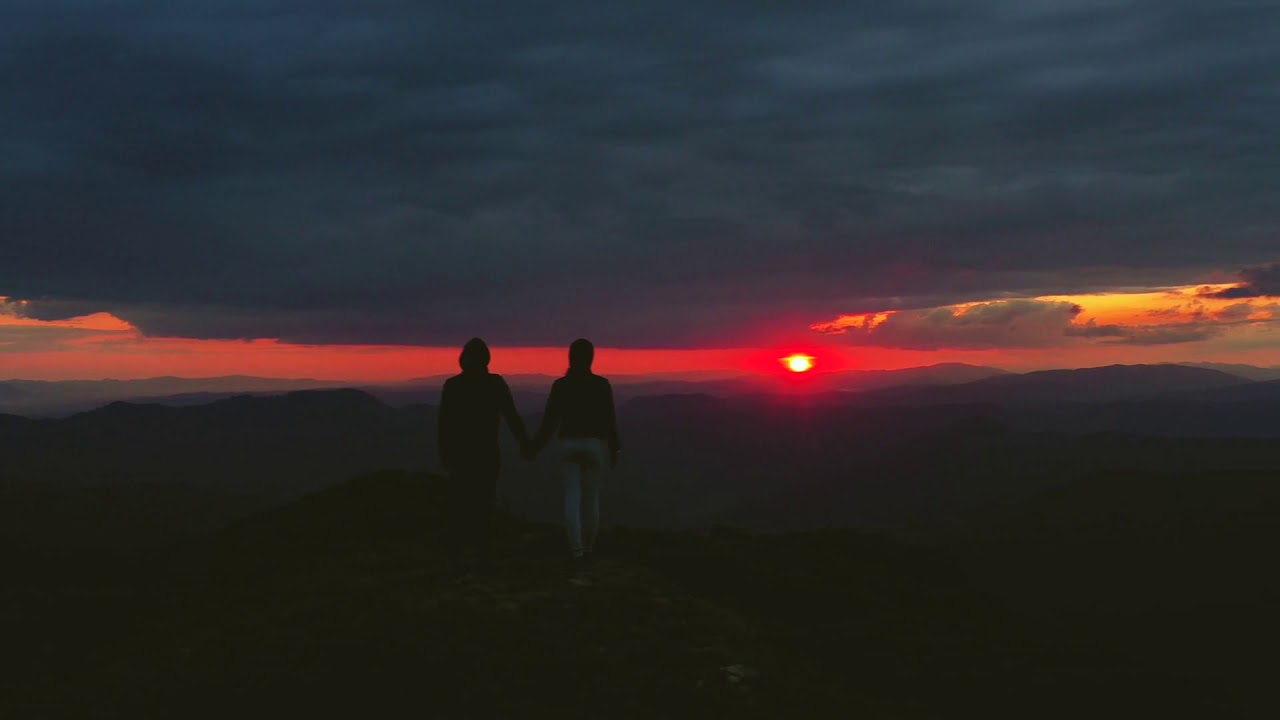 the man and woman standing on the mountain on a sunset background - YouTube