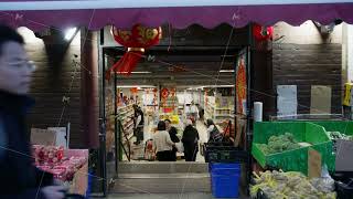 People shopping inside urban Chinese grocery store with red lanterns and fresh produce at its