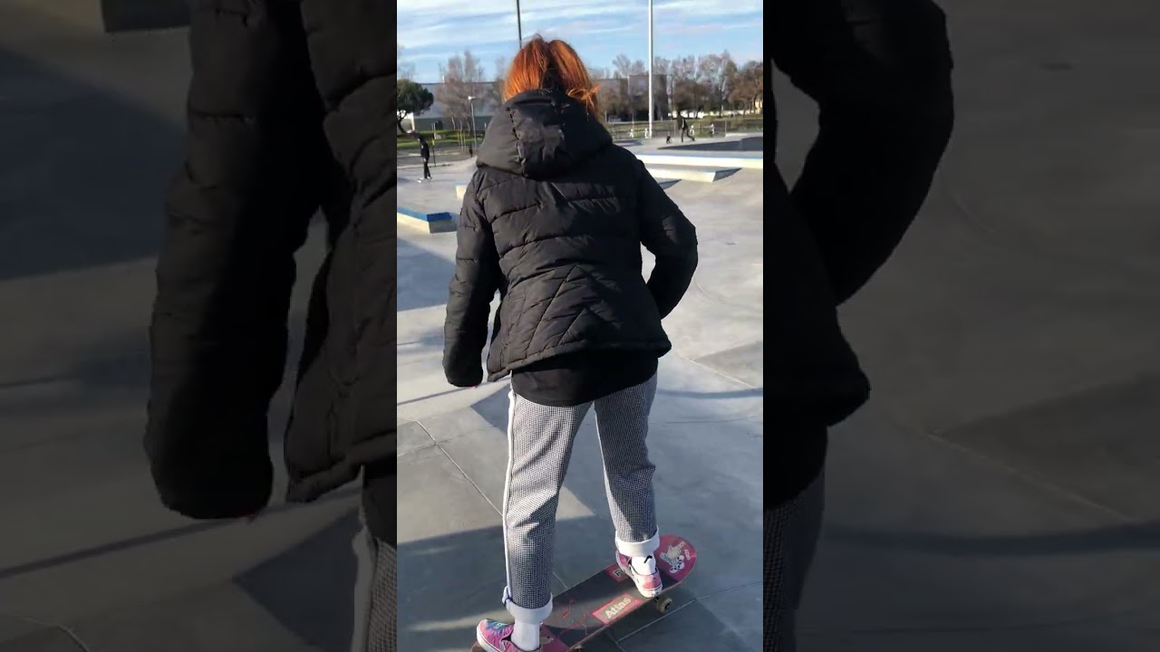Girl on skateboard rolls down ramp at skatepark then another skateboarder crashes into her