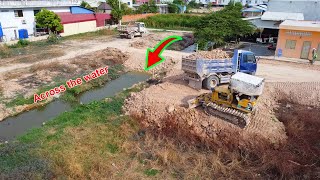 New delete old grass across the water by Komatsu D20P dozer with dump trucks unloading