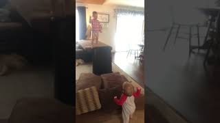 Kid jumps from top of couch onto cushions but baby brother gets in the way