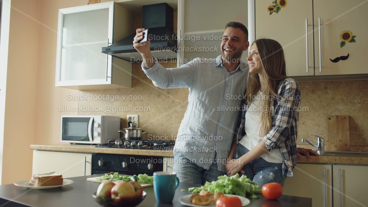 Young happy couple having online video chat in the kitchen at home