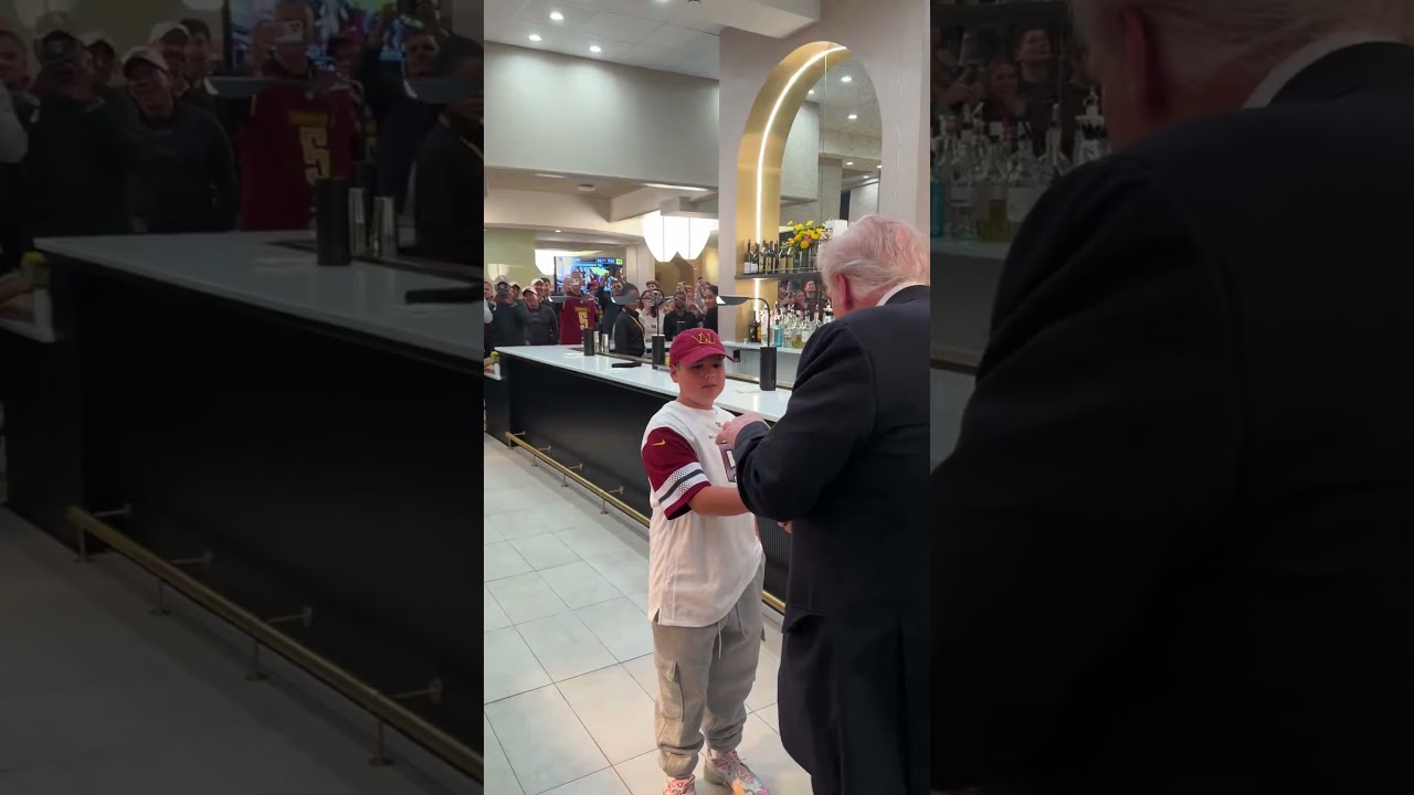 Trump hands a boy his presidential challenge coin as he’s leaving the Washington Commanders game