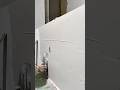 applying a thin layer of light grey plaster to a vertical wall using a flat metal trowel indoors