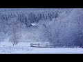 Snowflakes are falling on a log cabin close to a bridge over a frozen creek - nature relaxation