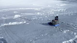 Boy rides sled down snow hill then hits a ramp and lands in lawn chair position