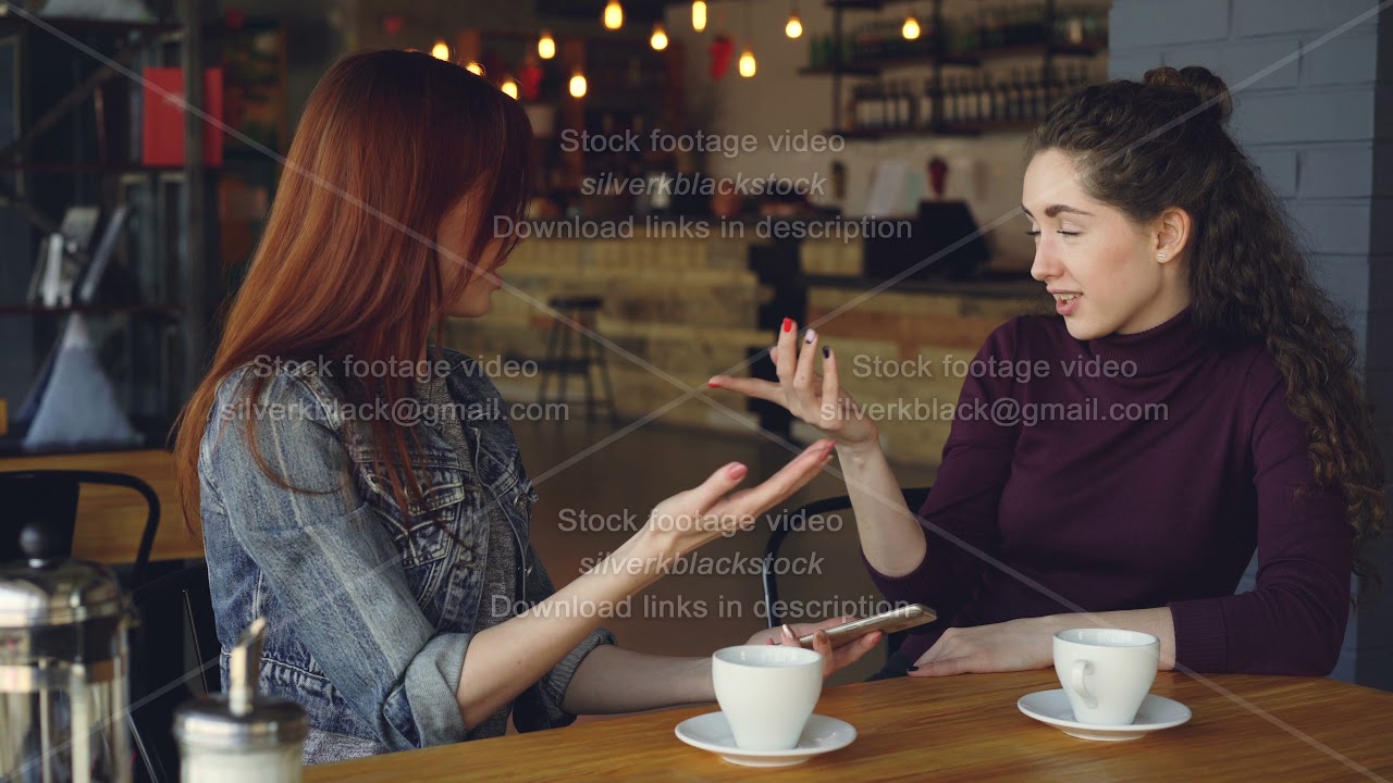 Young women are using smartphone, talking and doing high five while drinking tea in cafe in