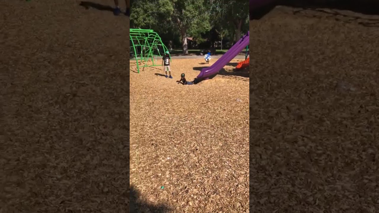 Little boy goes head first down purple slide at playground then faceplants and has woodchips on face