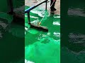 Flat squeegee spreads green epoxy smooth across floor