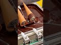 Machine dips waffle cones into flowing melted chocolate coating