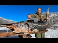 A giant sturgeon roasted under a barrel in a bonfire dinner in a snowy village