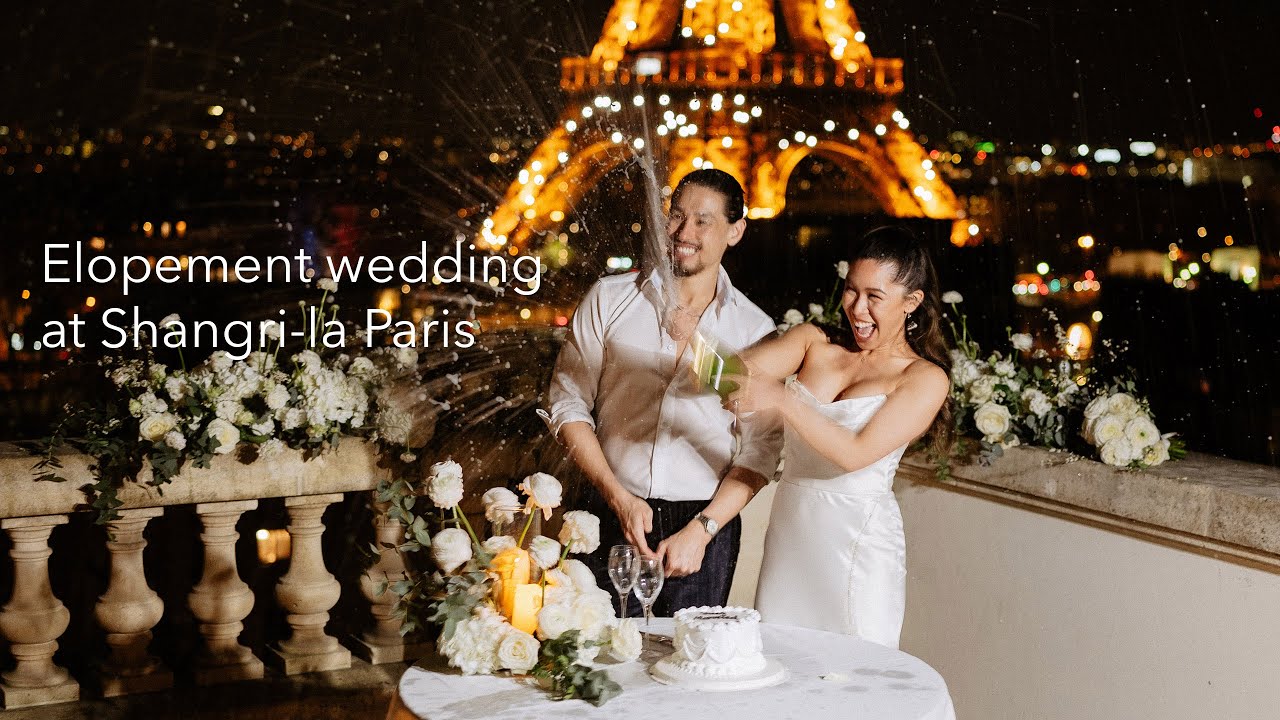 Bride and groom pop champagne on a flowered terrace with the Eiffel Tower glowing behind them