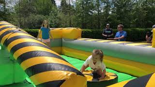 Girl gets hit on her back by swinging arm ride at the fair and launches into inflatable wall