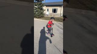 Boy wearing helmet rides scooter on street then does double jump and falls forward then faceplants