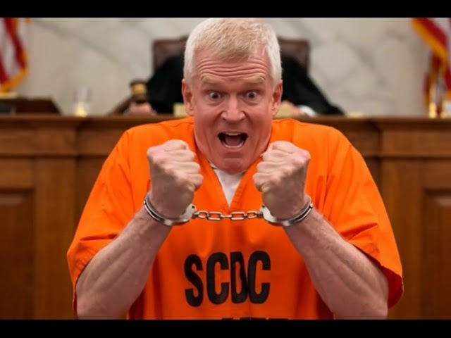 There is a man in an orange suit and handcuffed in the courtroom in the picture