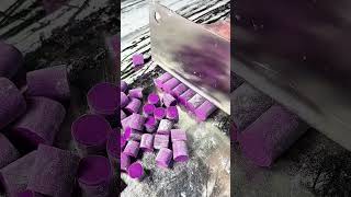 Slicing purple chalk sticks into small pieces using a large metal kitchen knife
