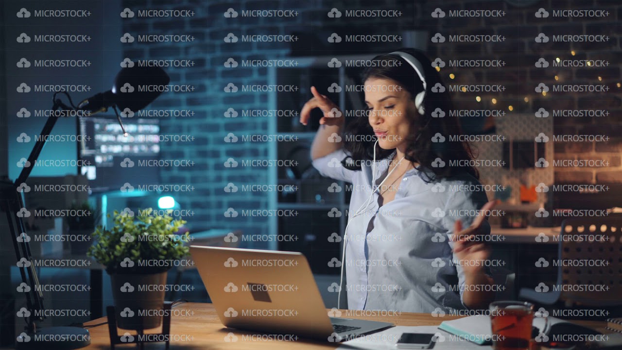 Woman typing on laptop listening to music in headphones in dark office ...