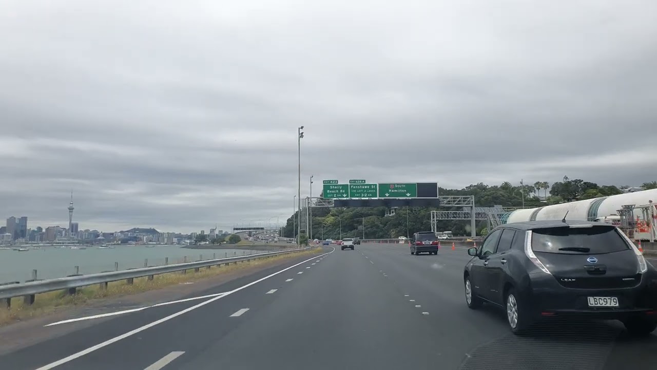 Auckland Motorway Drive With CBD Backdrop: Harbour Bridge And Water Views POV