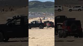 Guy on beach uses weight machine in back of pickup truck