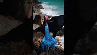 A hooded mermaid waits on the rocky shore as waves crash behind her. #mermaid #beach #h2o #siren