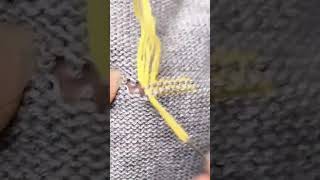 darning a small hole in a grey knitted fabric with a needle and yellow thread by hand carefully now