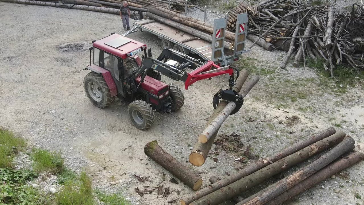 Baumstämme laden auf Tieflader mit Case 940 und Forstzange. Holz wird im Sägewerk weiterverarbeitet