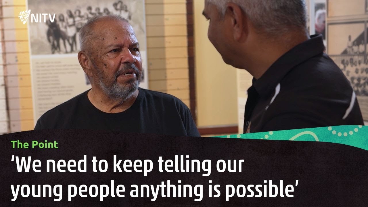 A still from NITV's The Point: a Cherbourg Elder talks with the reporter beside historical photographs.