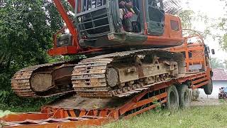 The process of lowering a Hitachi excavator from a self-loader.