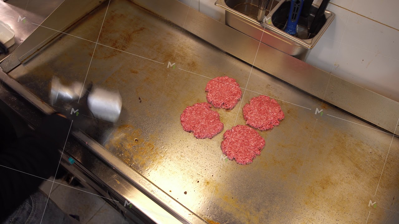 Professional cook preparing raw hamburger meat on a hot plate in commercial restaurant. Overhead