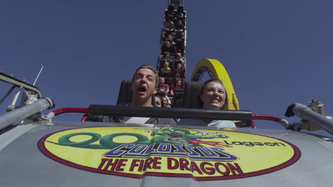 Slow motion shot of front seat of rollercoaster. Couple is screaming.