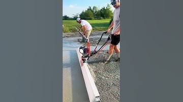 This man is leveling the cemented land with a straight piece of wood
