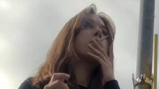 A girl in high heels is smoking at a bus stop and littering.