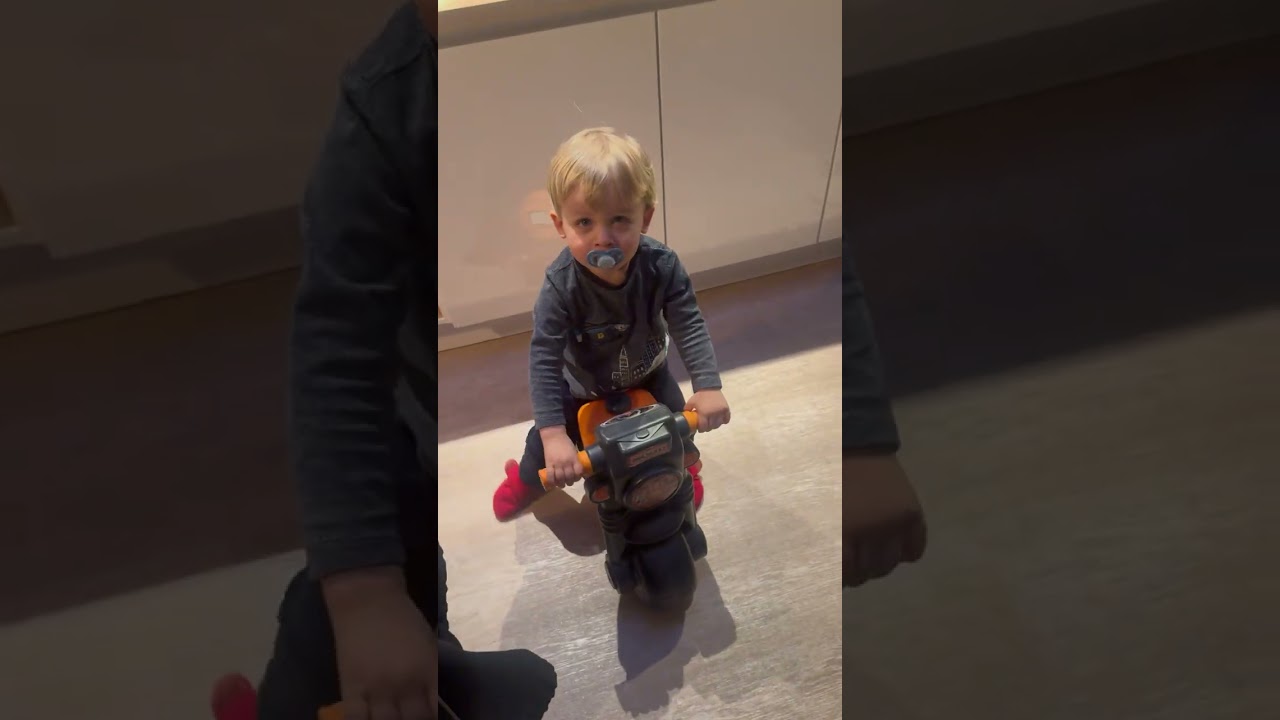 Boy rides toy motorcycle through house and kitchen then falls and bumps head on floor