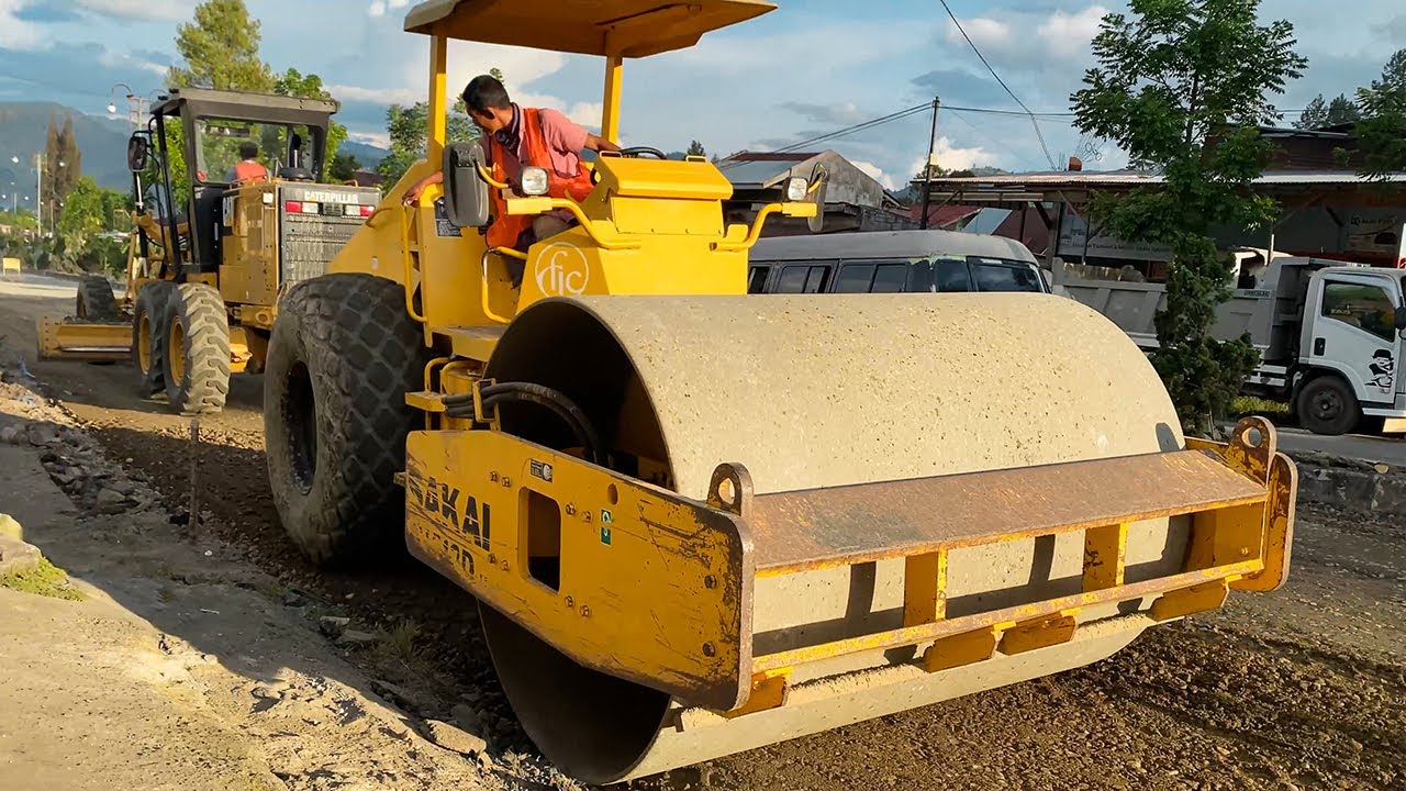 CAT 120K Grader, SAKAI SV512D Compactor & Dump Trucks Working to Construct Public Road