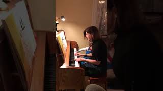 Woman plays piano while little boy sits beside her and falls off bench
