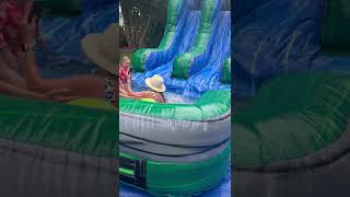 Woman holding Capri Sun and phone slides down inflatable water slide and crashes into kid