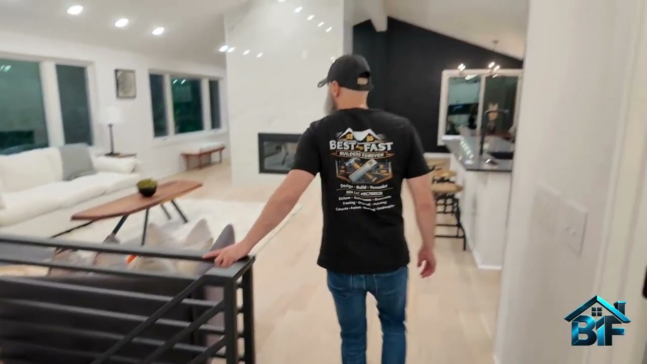 Video still: a Best and Fast team member walks through the renovated living room — white sectional, live-edge coffee table, marble fireplace and black slat wall