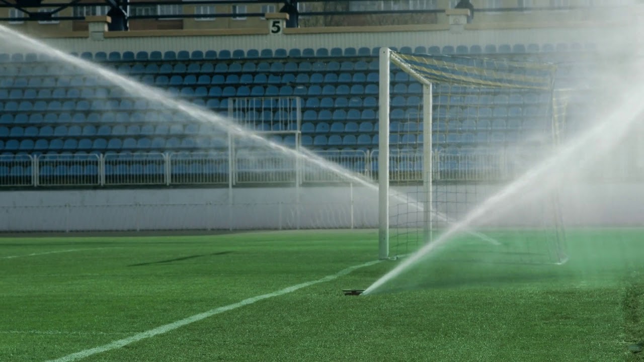water jets sprinkling on green grass of soccer stadium sports field