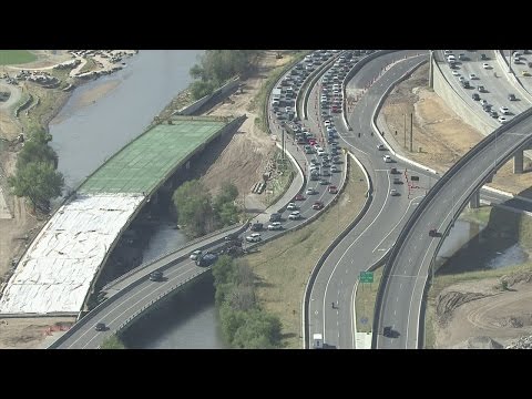 Tractor trailer carrying cars turns on side near I-25